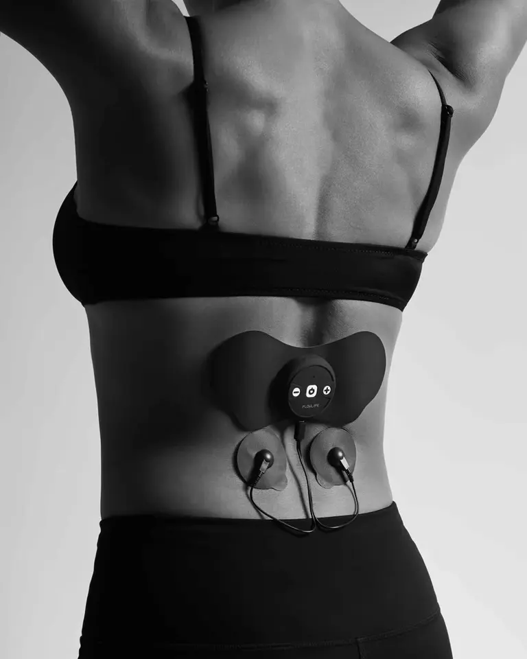 A woman with the Flowtens Connect device and electrode pads on her lower back for targeted nerve stimulation.