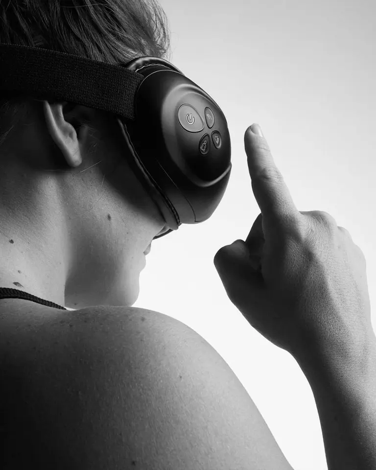 A person wearing black Flowpression Goggles, adjusting the side control panel for targeted eye massage and heat therapy.