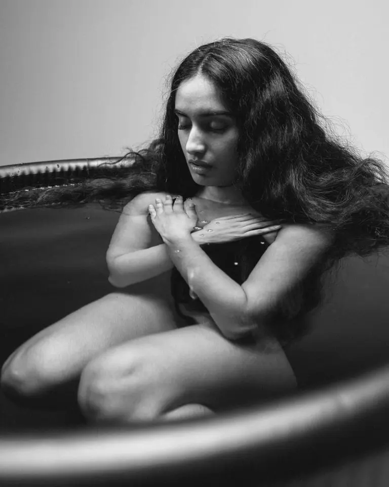 A woman kneeling in the Flowplunge Pro cold plunge tub for recovery, captured in a black and white studio photo.