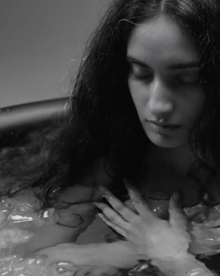 A woman submerged in the Flowplunge Go portable ice bath, resting her hands on her chest amidst floating ice.