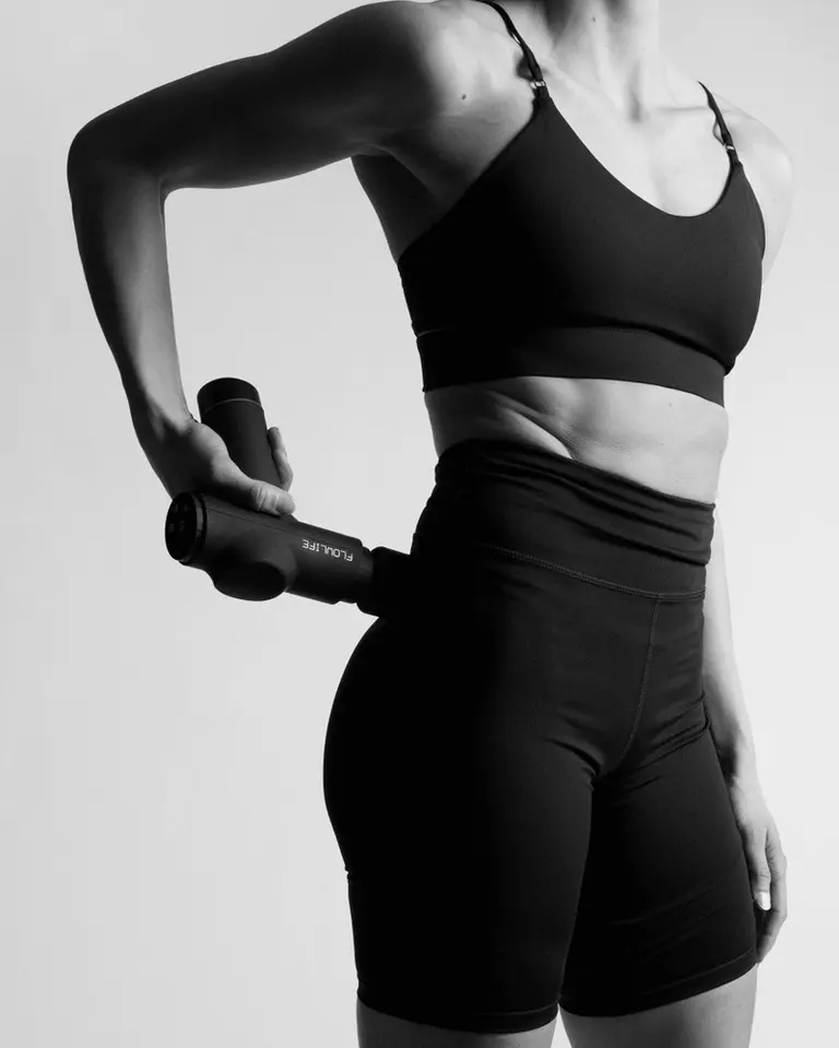 A user applies the black Flowgun Heat to gluteal muscles for recovery in a black and white studio photograph.