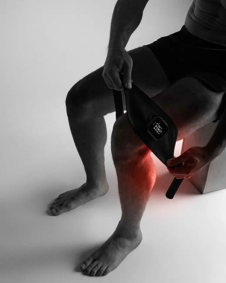 Flowtherma Spot applied to a knee using adjustable straps, showing the red light therapy glow for targeted recovery.