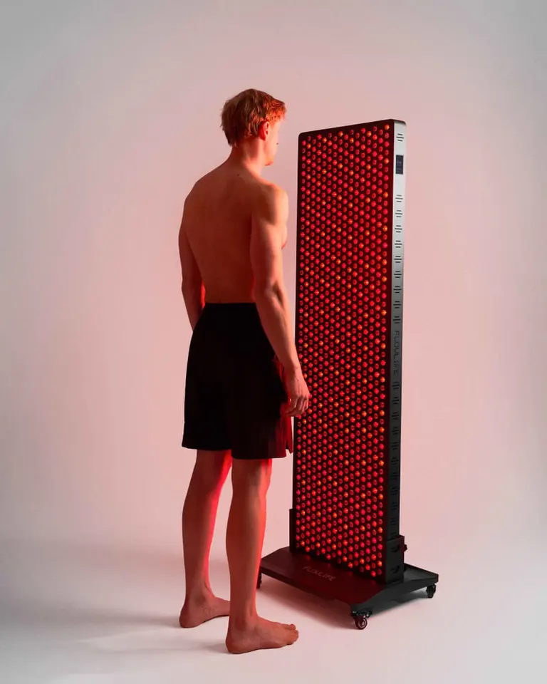 A man stands before the Flowlight 4300 Eight Waves red light therapy panel on a floor stand with wheels.