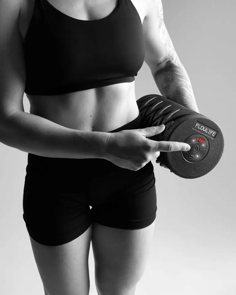 Woman in black sportswear pressing the power button on the black textured Flowroller Pro vibrating foam roller.