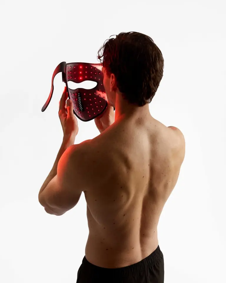 Rear view of a man holding the Flowlight Laser Mask Ultra Three Waves with glowing red laser LEDs for recovery.