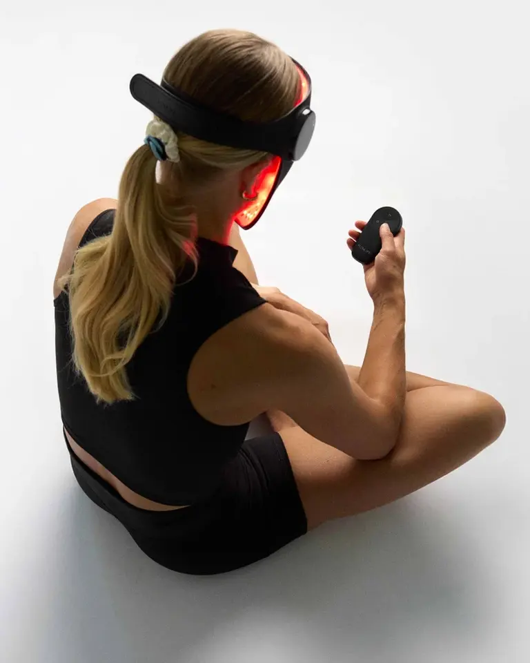 Woman using the Flowlight Laser Mask Ultra Three Waves and wireless controller for red light therapy from a rear angle.